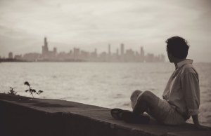 man sitting on ledge by water and a city