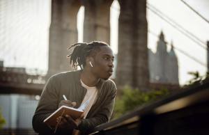 Man with earphone in journaling in front of a bridge