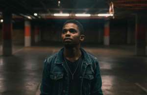 Man in black t shirt with denim jacket standing in dark empty parking garage.