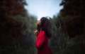 Woman in red dress looking up at blue sky in green brush.