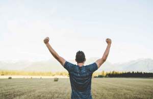 man holding arms up in field by mountains