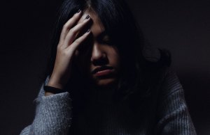 Woman in distress with her hand on her head in a dark room.