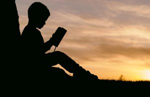 silhouette of child reading by sunset.