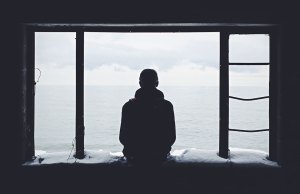 shadowed image of man sitting in window looking our at the ocean.