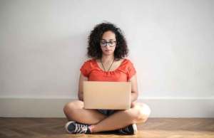 woman in orange shirt on floor with laptop