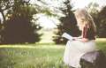 woman in white skirt reading book in grass