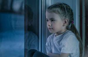 girl with braided hair in white crew neck t shirt and tiara looking out the window.