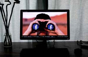 computer screen with man holding binoculars with facebook logo