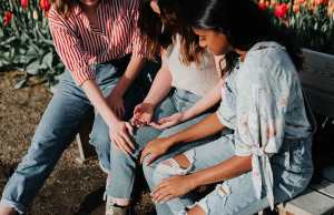 3 people in jeans sitting on bench outside