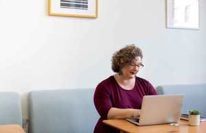 Woman in red shirt sitting at table on laptop.