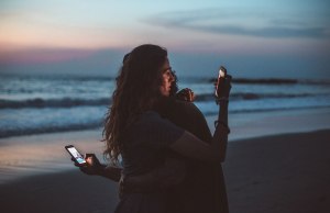 two people hugging and holding cell phones at sunset