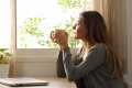 Woman sitting at a kitchen table with a coffee mug in her hands, looking out the window