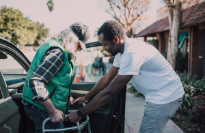 Volunteer helps elderly man with walker