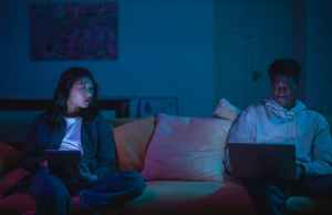 Couple sitting on couch looking at phone and computer.