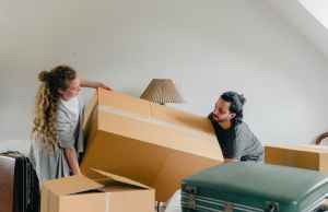 Man and woman carrying a cardboard box- looks to be in the process of moving.