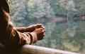 Persons arms leaning on a ledge holding their hands overlooking an outdoor tree scene.