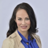 Woman wearing light brown jacket and blue shirt, with dark hair