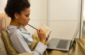 Ethnic woman sitting in bed reading and using her laptop