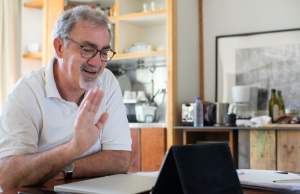 Man sitting at a table waving at tablet screen