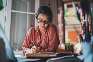 Woman in a pink shirt studying in her kitchen with the doors and windows open behind her