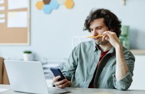 Young white man browsing on his phone instead of working