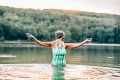 Older woman in a blue swimsuit, gloves, and a hat standing in cold lake